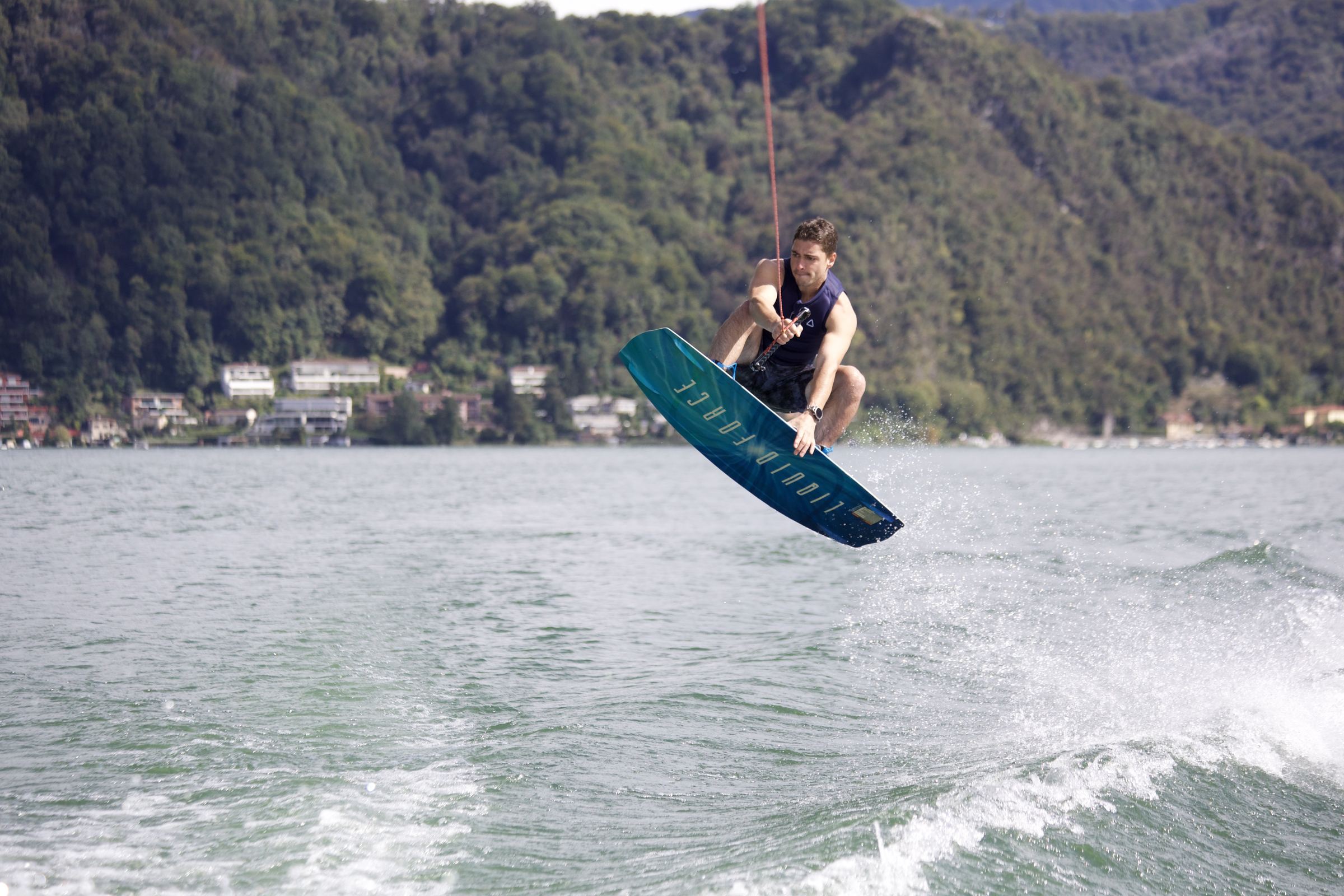 Un rider di Good Vibes Lake salta la scia col wakeboard sul Lago di Lugano, sullo sfondo la collina